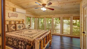 A cabin with a wooden ceiling, a bed with a quilt, and large windows with blinds. - River Haus - Riverfront Luxury Lodge in Downtown Helen (Helen)