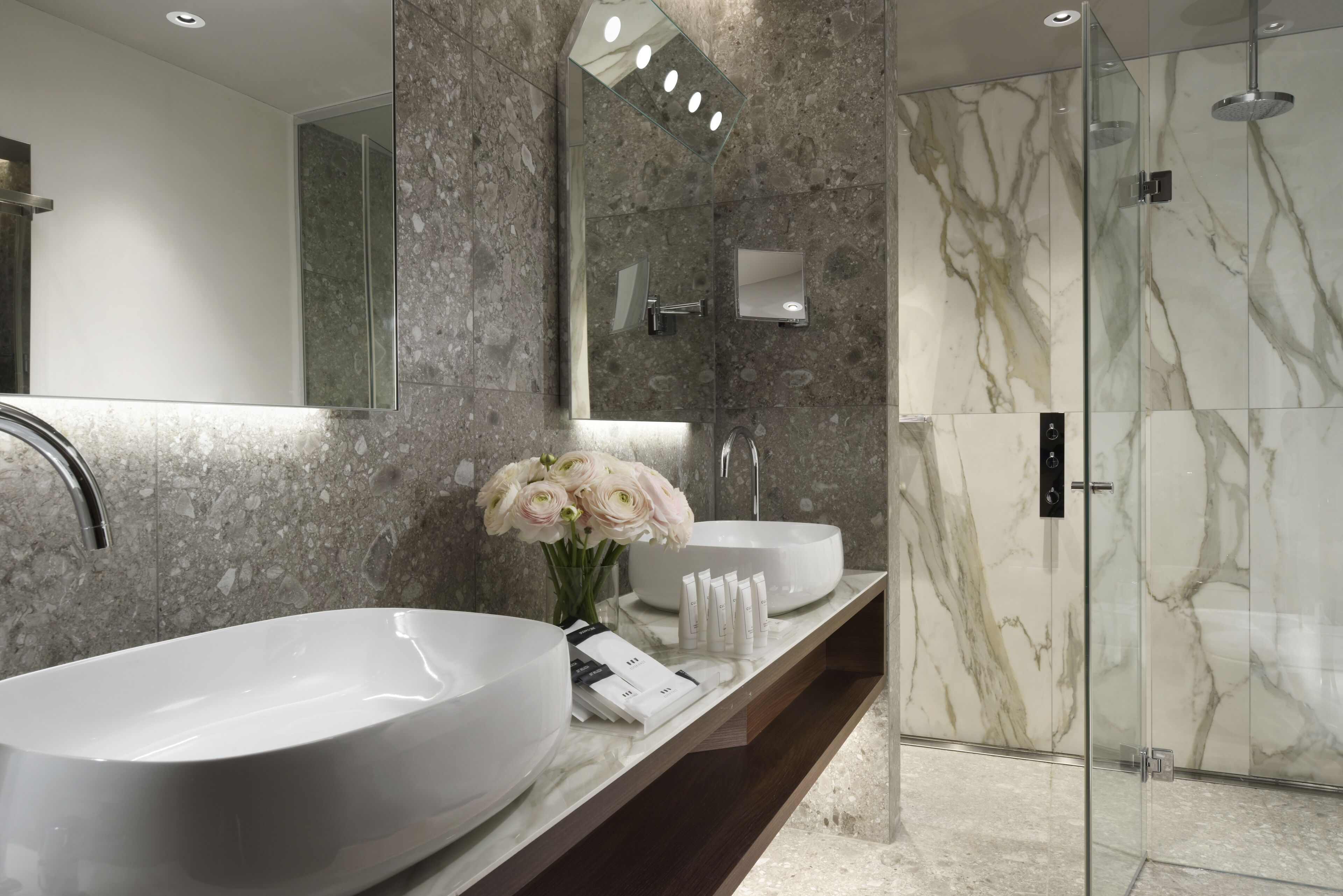 A modern bathroom with a large white sink, a mirror, and a glass-enclosed shower.