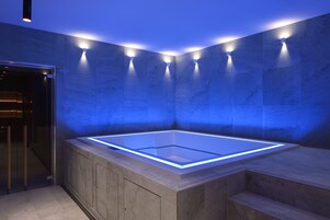Una moderna spa con vasca idromassaggio in vetro, pavimento in legno e illuminazione blu soffusa.