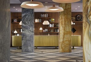 A lobby with marble columns, a checkered floor, and a wooden reception desk with bookshelves.