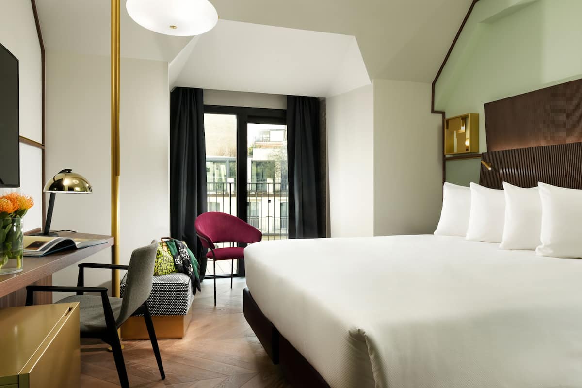 Une chambre d’hôtel avec un grand lit, un bureau avec une lampe, une chaise et une vue sur la ville par la fenêtre.