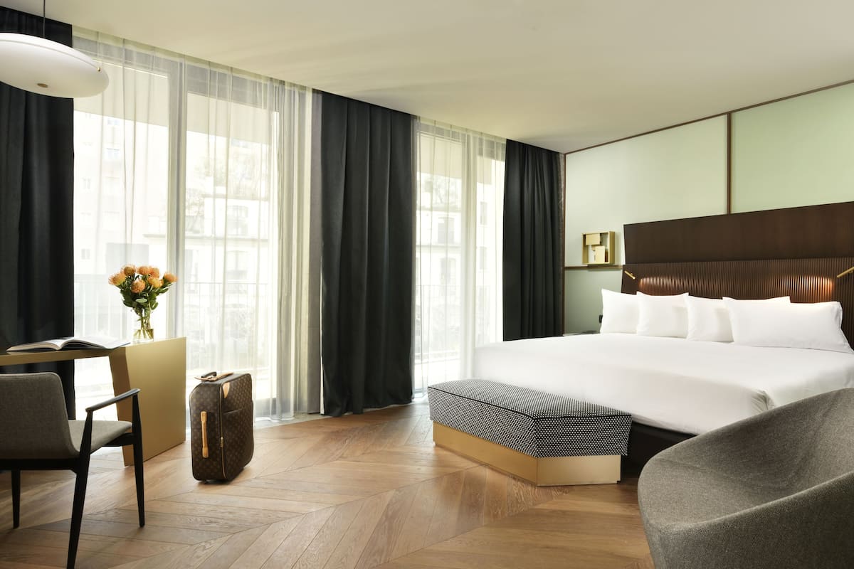 Une chambre d’hôtel avec un grand lit, un bureau avec une chaise, une valise et un vase de fleurs.