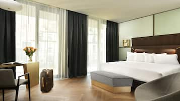 Ein Hotelzimmer mit einem großen Bett, einem Schreibtisch mit Stuhl, einem Koffer und einer Blumenvase.