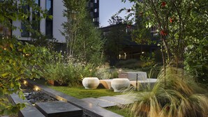 Een aangelegde tuin met een waterpartij, zitplekken en moderne architectuur op de achtergrond.