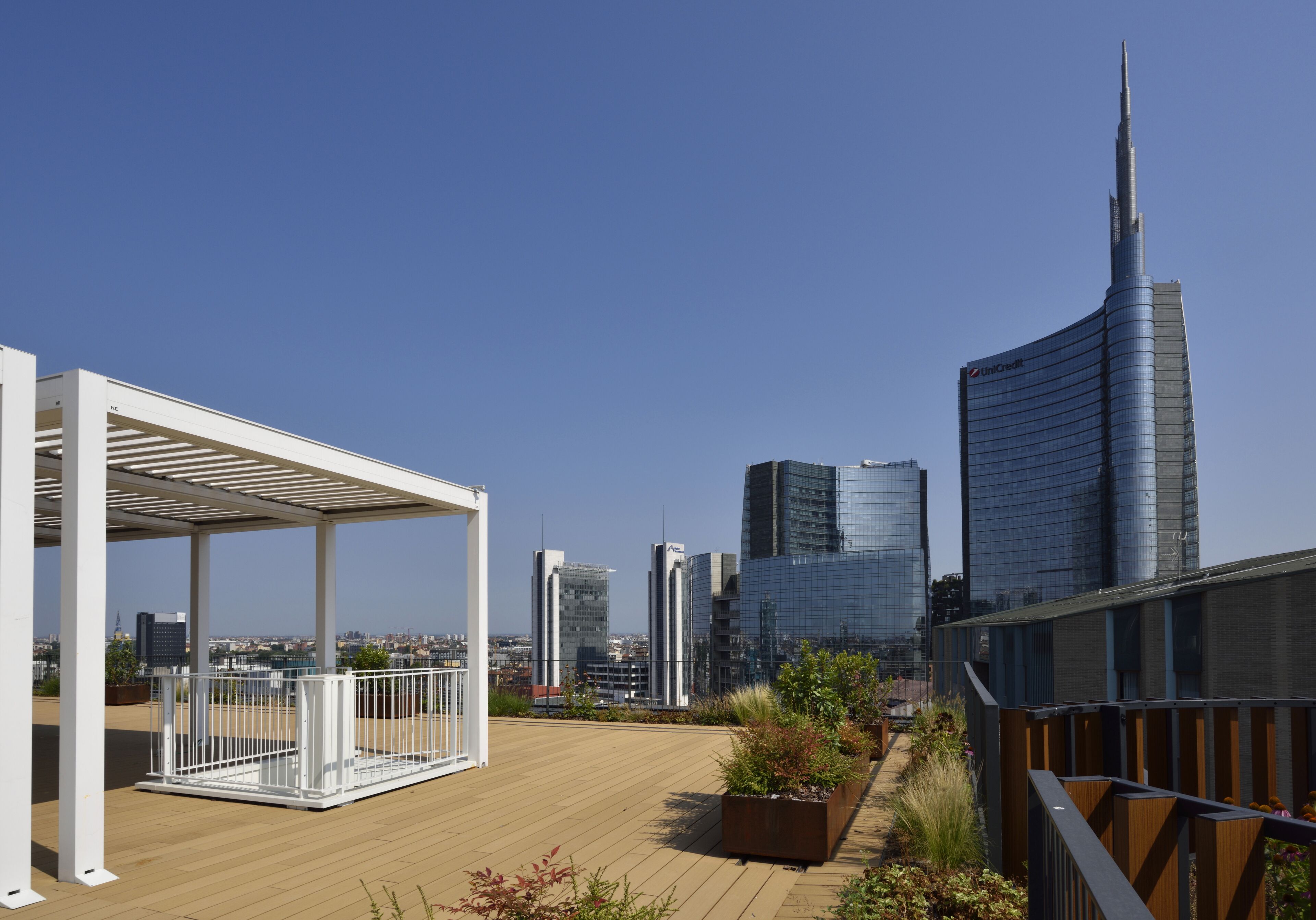 A rooftop terrace with a pergola, planters, and a view of the city skyline including a prominent skyscraper.
