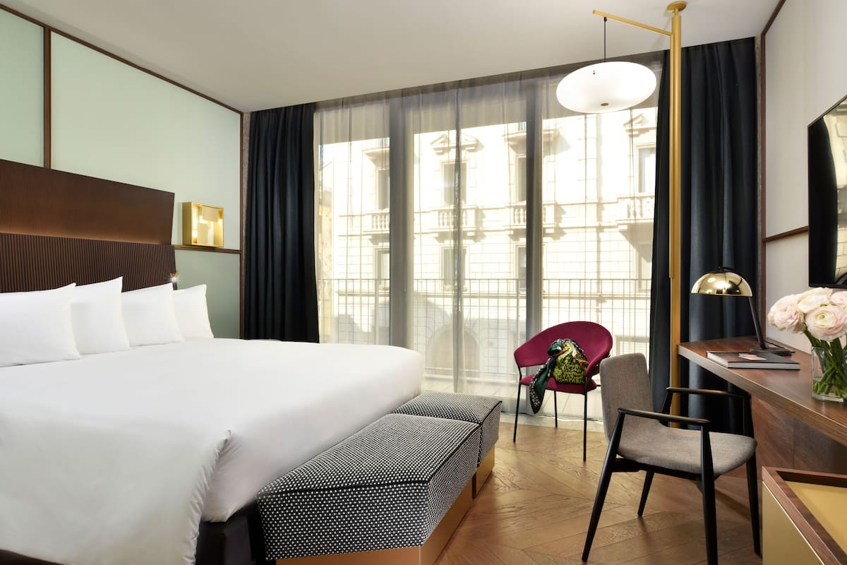 Une chambre d’hôtel avec un grand lit, un bureau avec une lampe, une chaise et un banc.