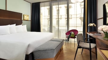 A hotel room with a large bed, a desk with a lamp, a chair, and a bench.