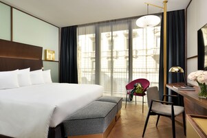 Habitación de hotel con una cama grande, un escritorio con lámpara, una silla y un banco.