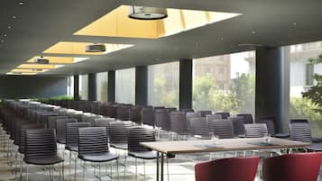 Un salón de conferencias con filas de sillas y mesas, ventanas amplias y un diseño de techo moderno.