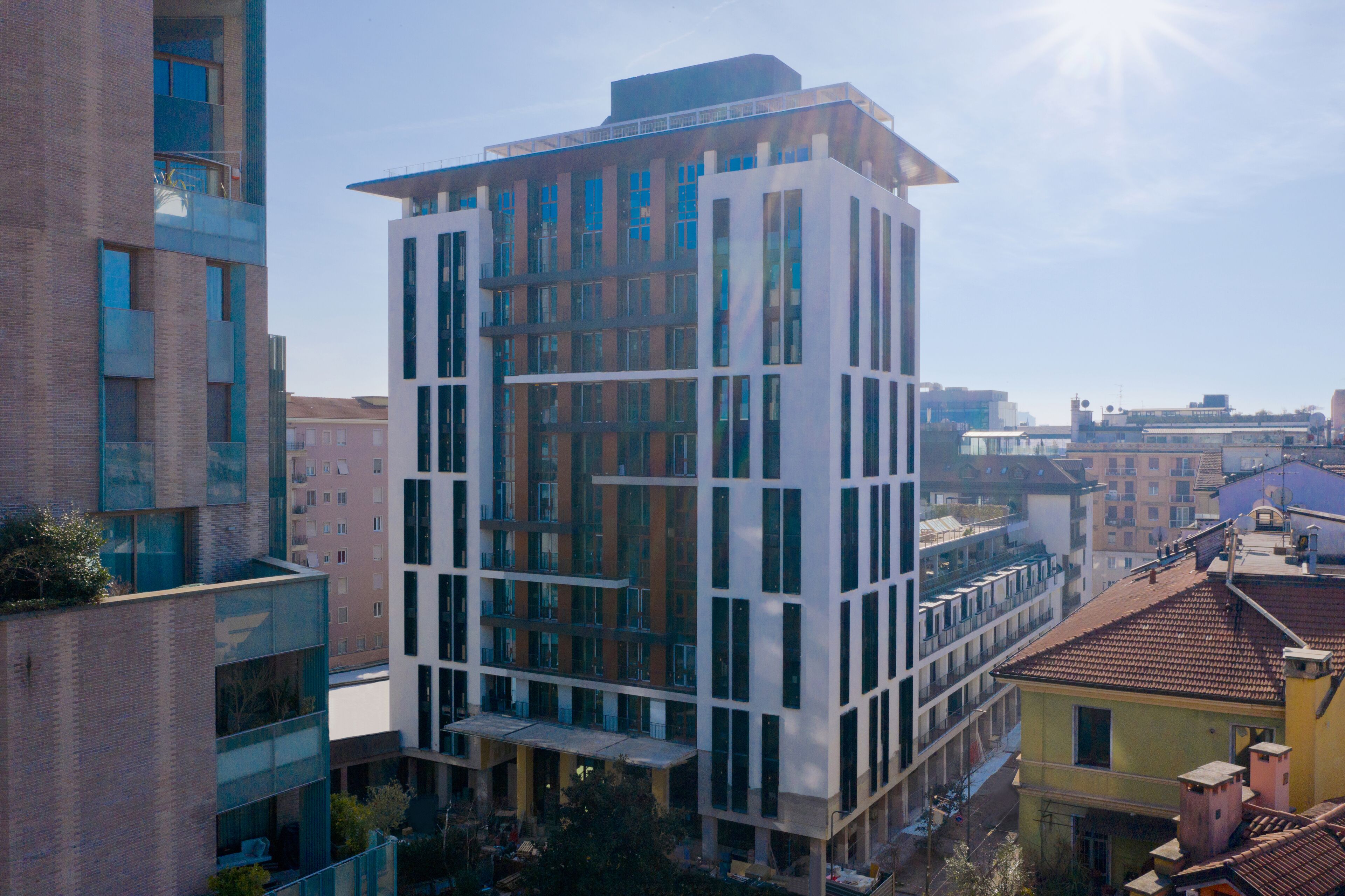Un edificio moderno de varios pisos con grandes ventanales y techo plano, rodeado de otros inmuebles.