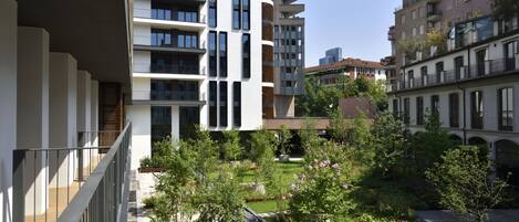 A modern apartment building with balconies, a courtyard with greenery, and a clear sky.