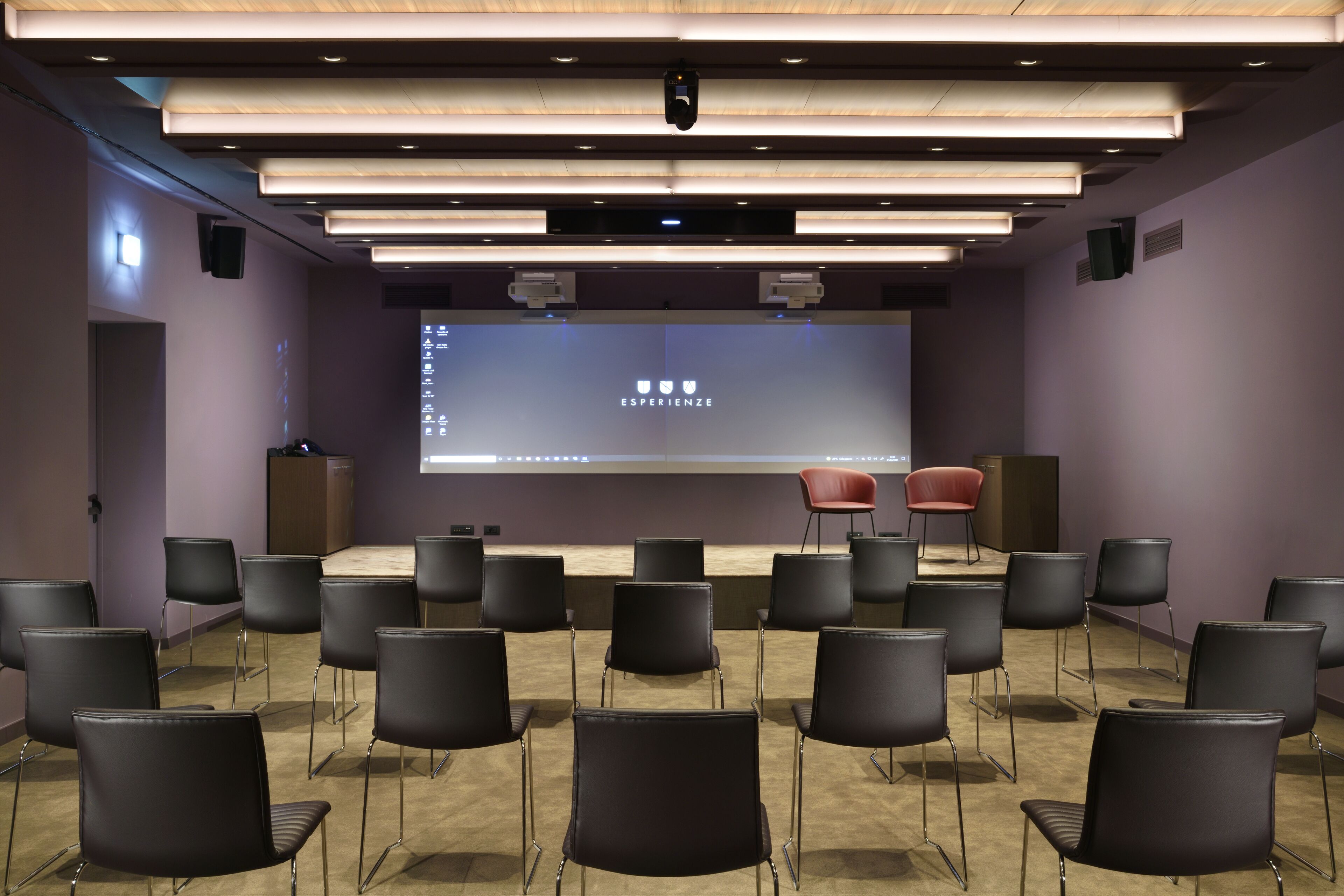 A conference room with a stage, a large screen, and multiple chairs arranged in rows.