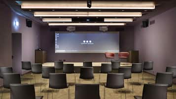 A conference room with a stage, a large screen, and multiple chairs arranged in rows.