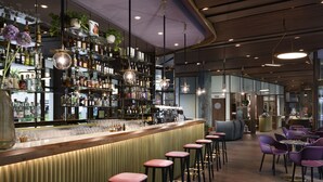 Een bar met een houten toonbank, meerdere barkrukken en flessenkasten.