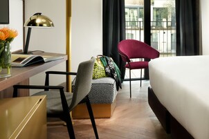 Una camera d'albergo con un letto, una scrivania con lampada, una sedia, un tavolino e una finestra con tende.