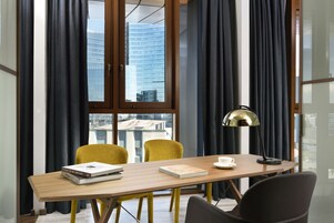 A modern room with a wooden table, two yellow chairs, a black lamp, and a view of a cityscape through large windows.
