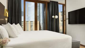 Een moderne hotelkamer met een groot bed, een flatscreen televisie en uitzicht op een stadsgezicht door middel van kamerhoge ramen.