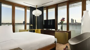 Een moderne hotelkamer met een groot bed, een bureau met een flatscreen televisie, een stoel en uitzicht op de stad.