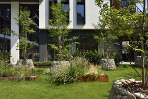 A modern building with large windows and a well-maintained garden with various plants and trees.