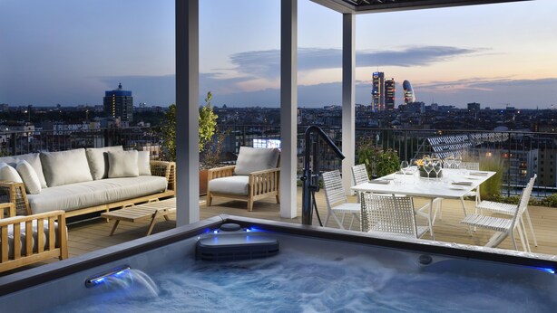 Een dakterras met een jacuzzi, een zithoek en een eethoek, met uitzicht over de stad.