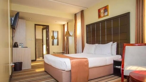 A hotel room with a large bed, a desk with a chair, a TV mounted on the wall, and a window with curtains. - Seeworld Adventures Car Hire (Nairobi)