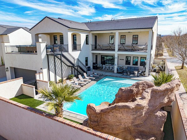 A two-story house with a swimming pool, outdoor seating, and a large rock feature. - 5 Suites, Private Pool, 2 Hot Tubs for 19, 2 Fire Pits, 2 Fridges Sleeps 30 (Hurricane)