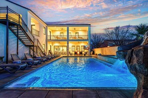 A multi-story building with a swimming pool, outdoor seating, and a waterfall feature. - 5 Suites, Private Pool, 2 Hot Tubs for 19, 2 Fire Pits, 2 Fridges Sleeps 30 (Hurricane)