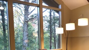 A cozy living room with a large window, a brown leather sofa, a chessboard, and a lamp. - Green Mountains 4BR House (Peru)