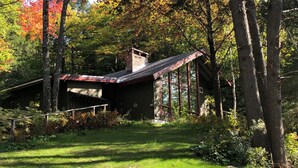 A rustic cabin with a sloped roof, surrounded by dense forest and a well-maintained lawn. - Green Mountains 4BR House (Peru)