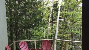 A wooden deck with red Adirondack chairs and a small table, surrounded by dense forest. - Green Mountains 4BR House (Peru)