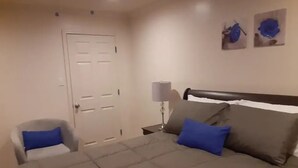 A bedroom with a bed, a chair, a nightstand, and a door.