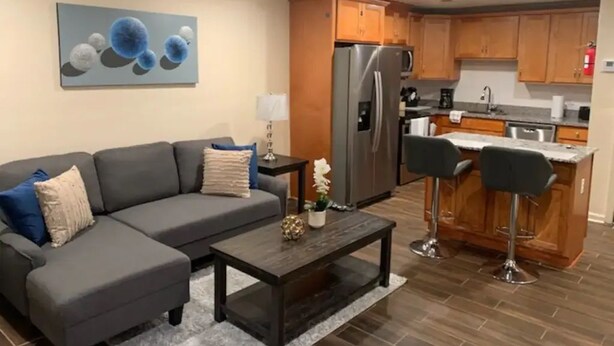 A modern kitchen with wooden cabinets, a stainless steel refrigerator, and a bar area with stools.