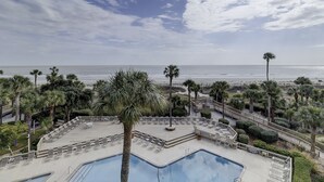 A pool area with lounge chairs and a view of the beach.