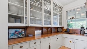 A kitchen with white cabinetry, a wooden countertop, and a window with a view of greenery. - "SABINO" 1 Bdrm Suite (Phippsburg)