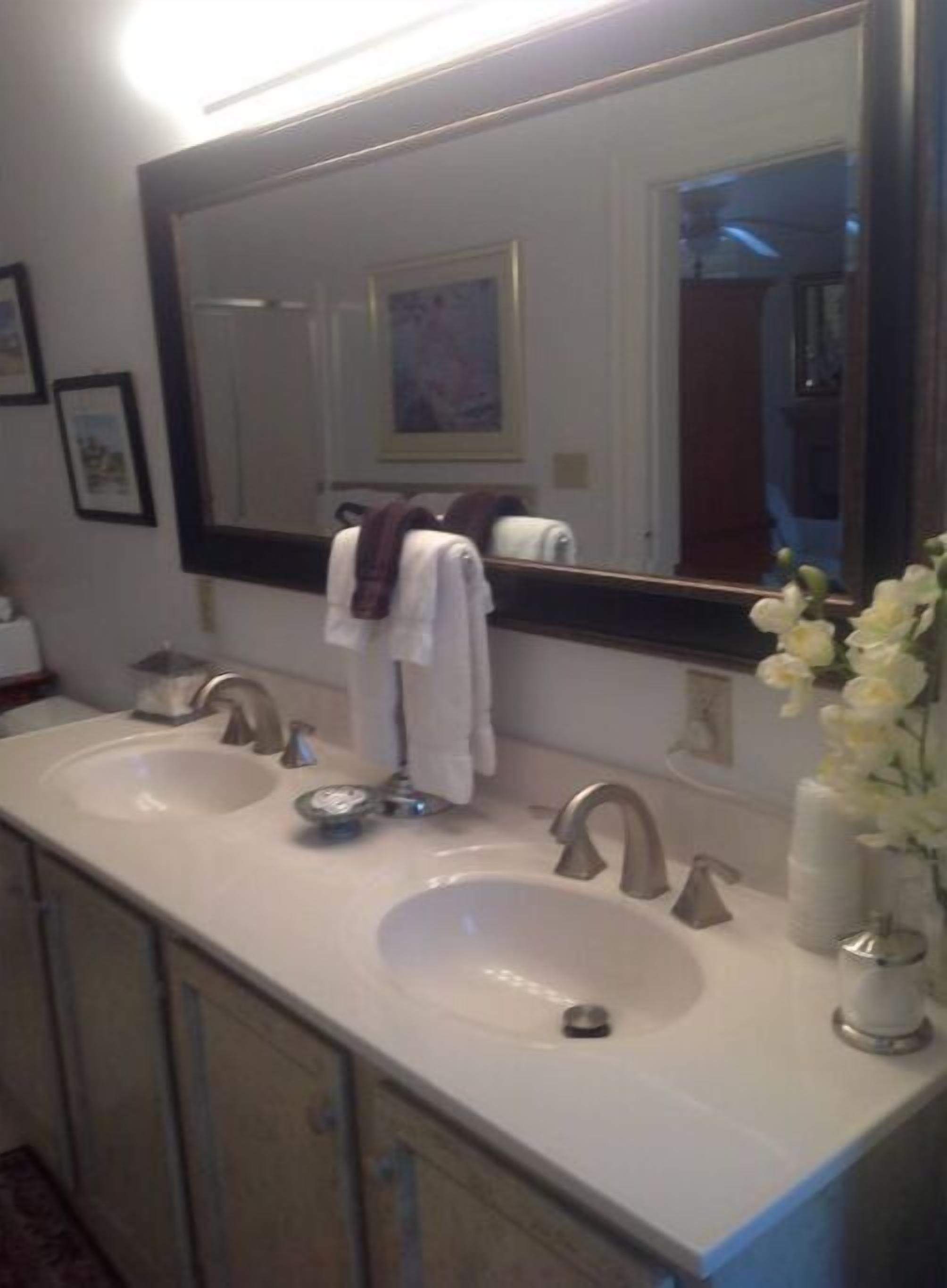 A bathroom with a double sink, a large mirror, and a vase with flowers.