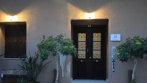 Un edificio con una puerta marrón oscuro, número 14, y una pequeña señal encima. Hay plantas en macetas frente a la puerta.