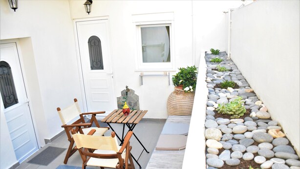 Un pequeño patio con una mesa y sillas de madera, una planta en maceta y un jardín de rocas.