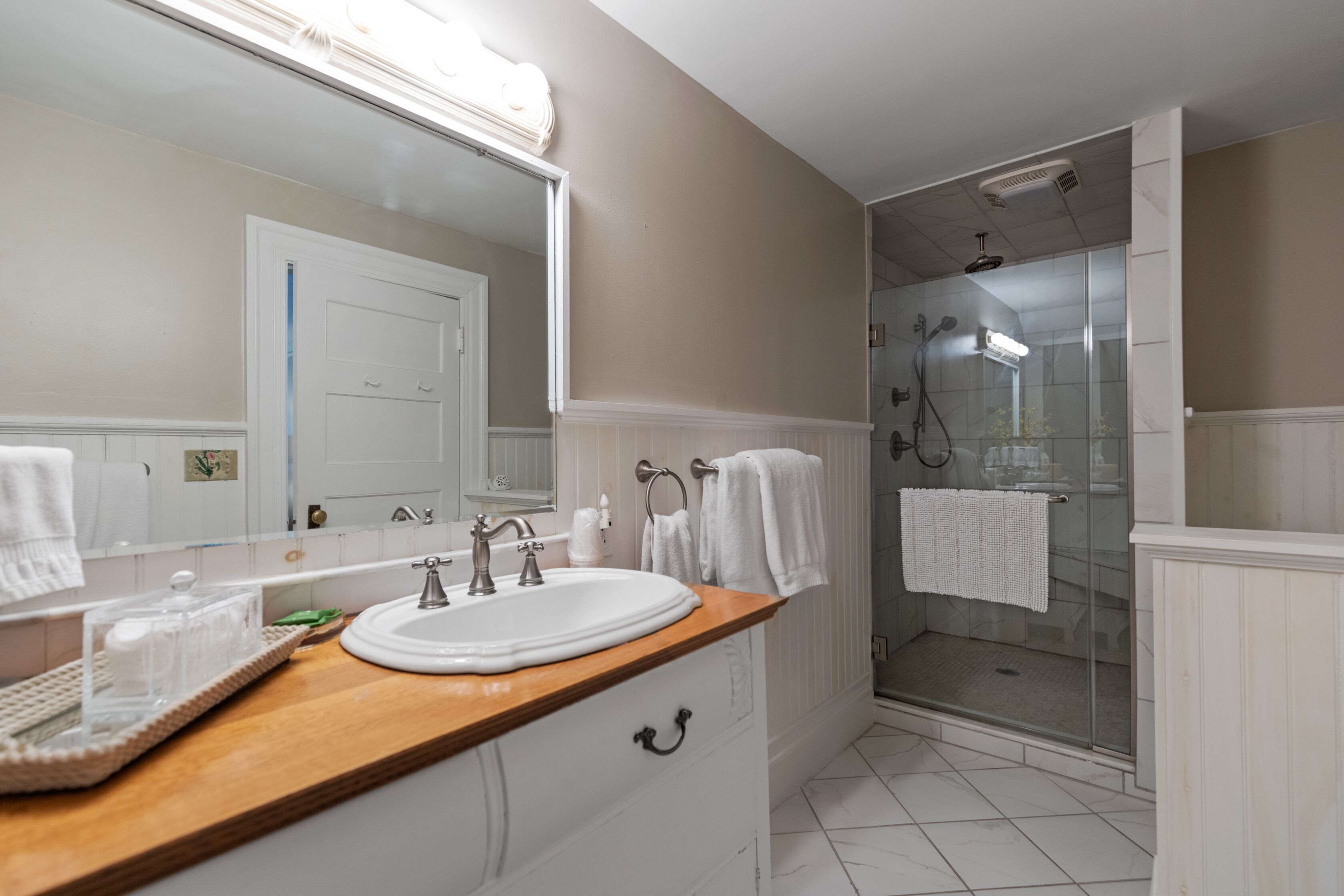 A bathroom with a wooden vanity, a white sink, a large mirror, and a glass shower enclosure.