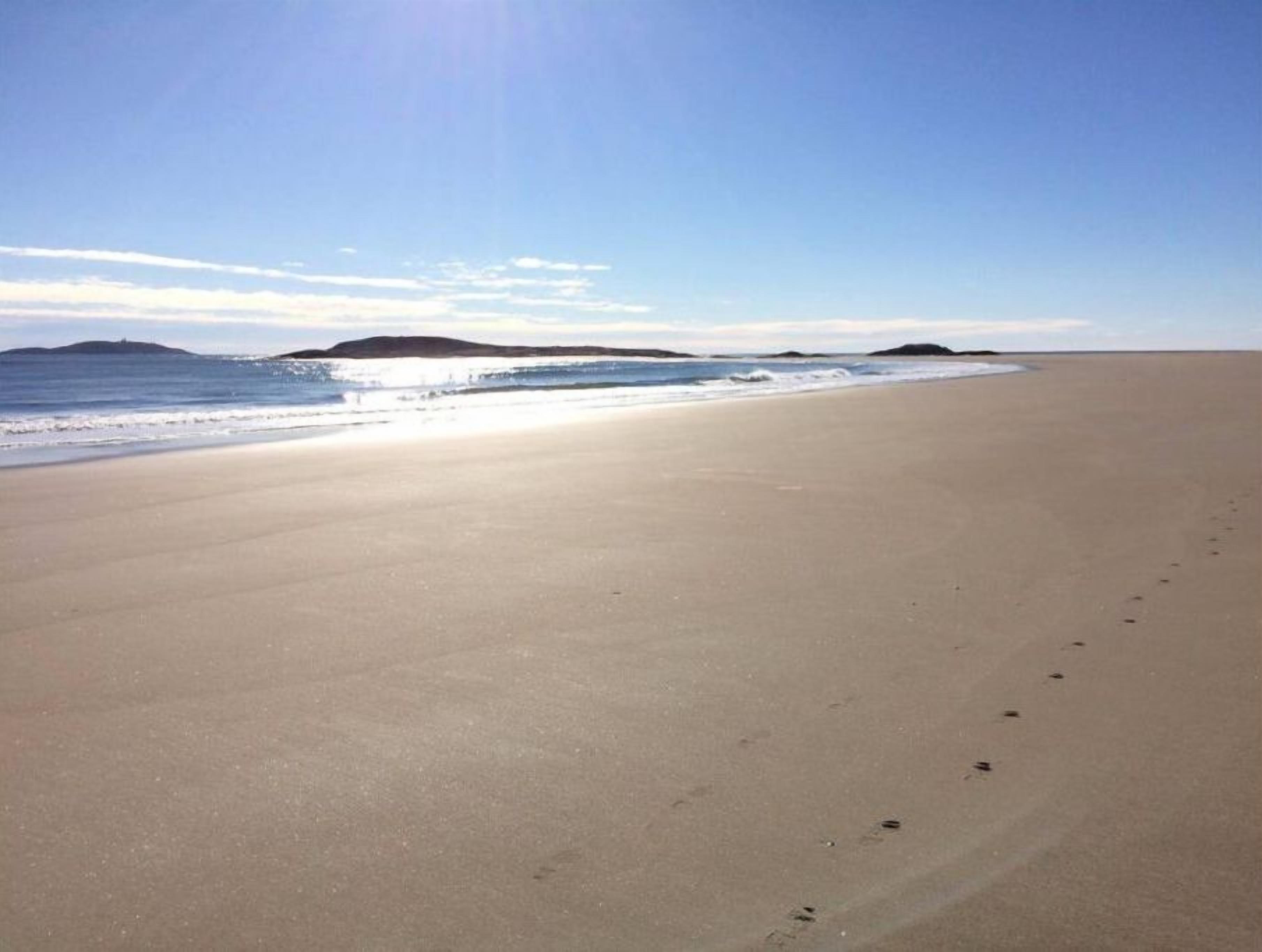 Ampia spiaggia deserta, cielo sereno e coste visibili in lontananza.