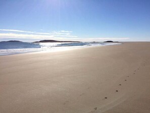 Une vaste plage déserte, sous un ciel dégagé, avec des reliefs lointains à l’horizon.