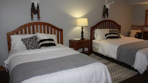 Een hotelkamer met twee houten bedden, een nachtkastje met een lamp en decoratieve wandkunst.