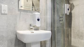Een moderne badkamer met een douchecabine, een wit wastafelmeubel en een handzeepdispenser.