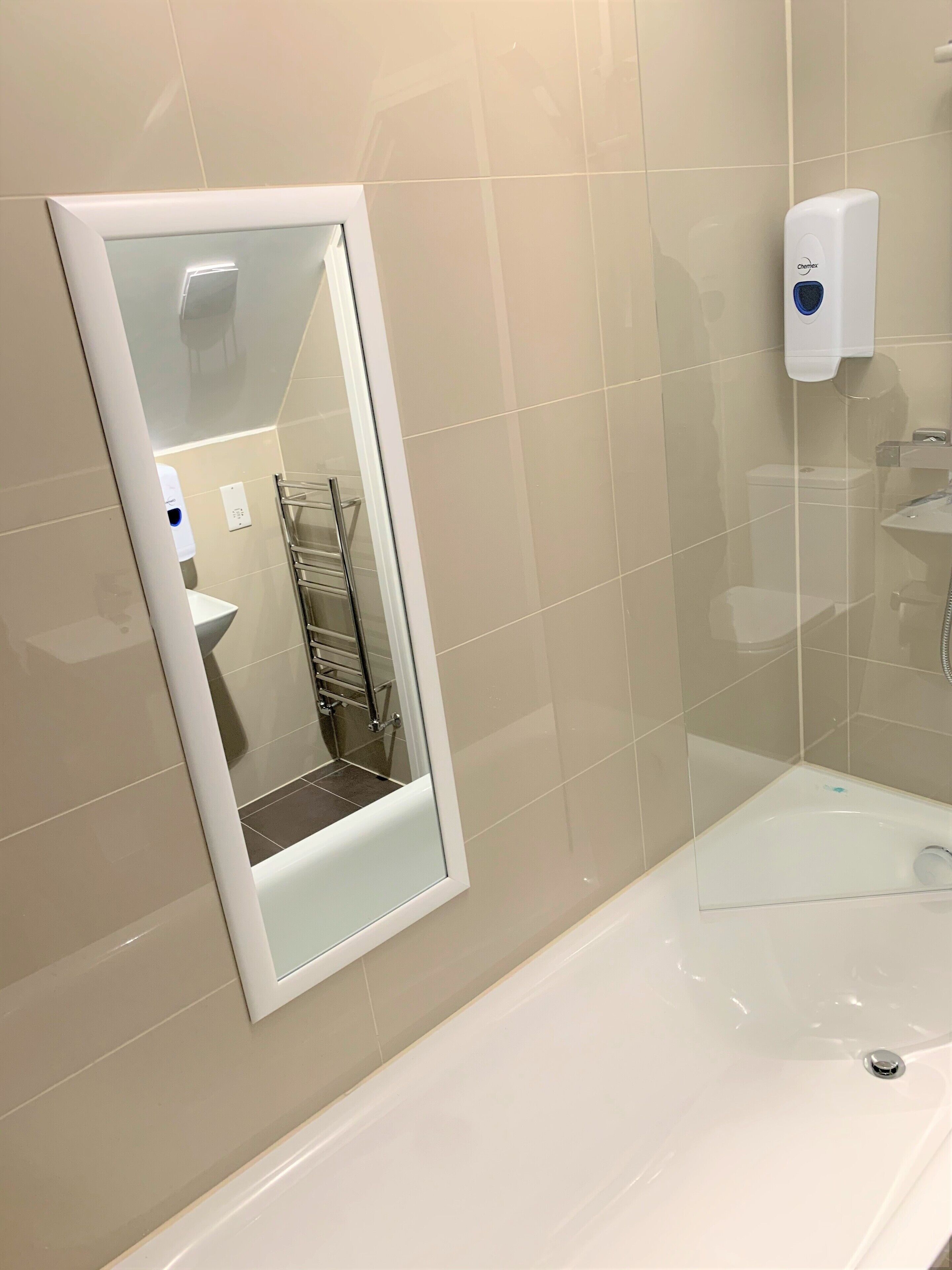 A bathroom with a large mirror, a hand dryer, and a bathtub.