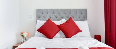 Un lit bien fait, avec une literie blanche et rouge, une tête de lit grise à motifs et un tableau sur le thème de la forêt accroché au-dessus.