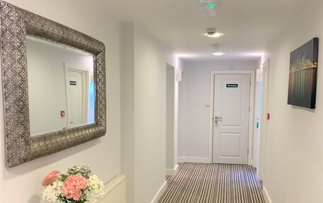 A hallway with a striped carpet, a mirror with a decorative frame, a vase with flowers, and a private door at the end.