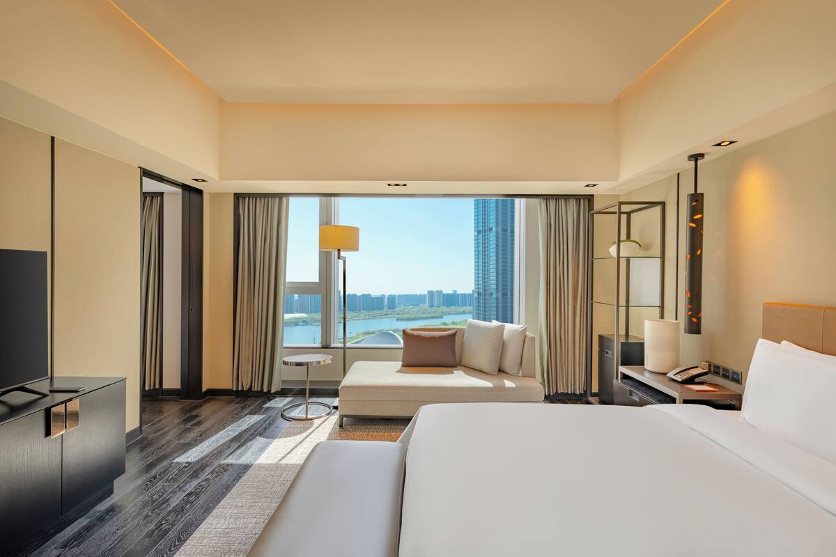 Une chambre d’hôtel moderne, dotée d’un grand lit, d’un canapé, d’un bureau et offrant une vue sur le paysage urbain.