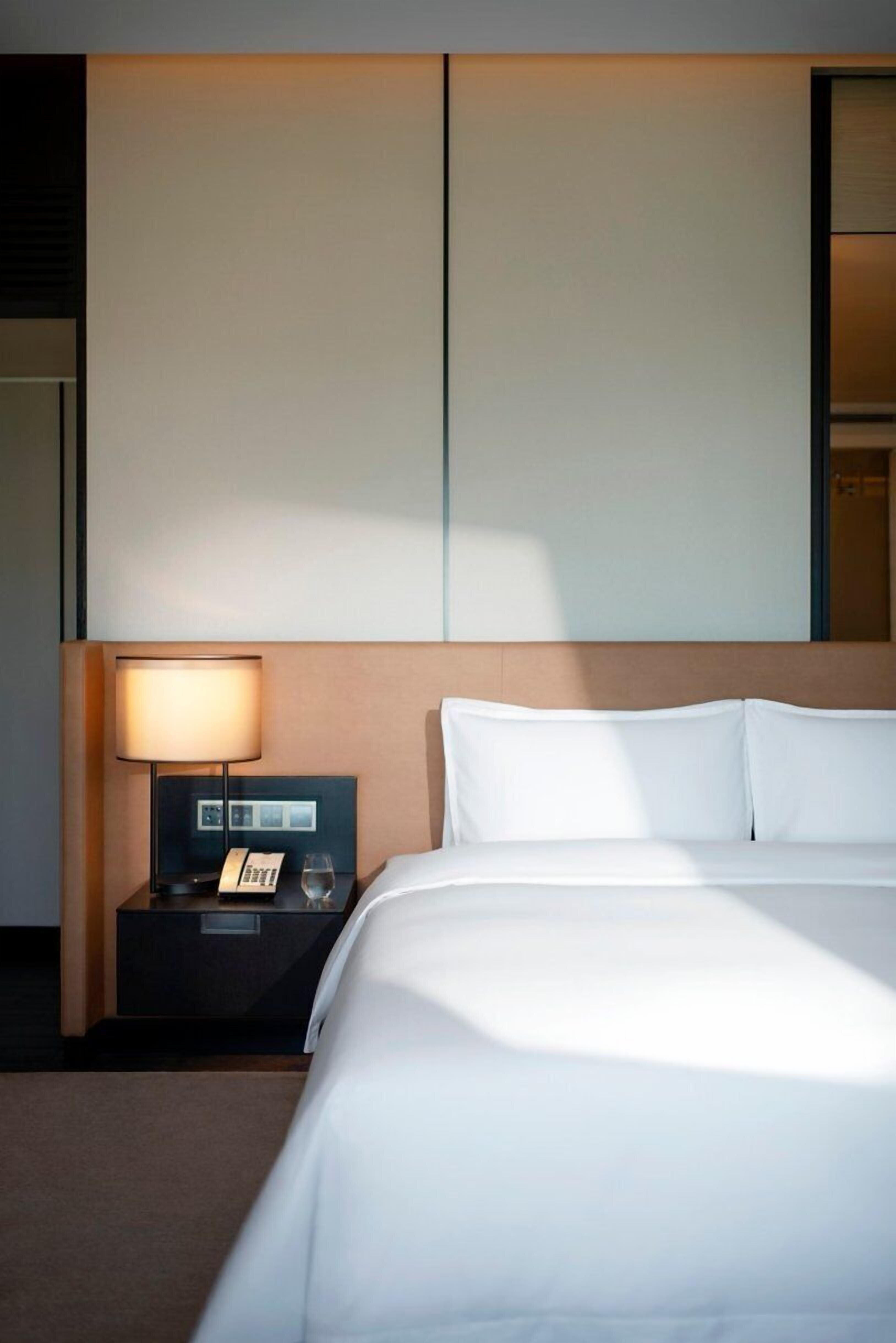A hotel room with a large bed, a bedside table with a lamp, and a phone.