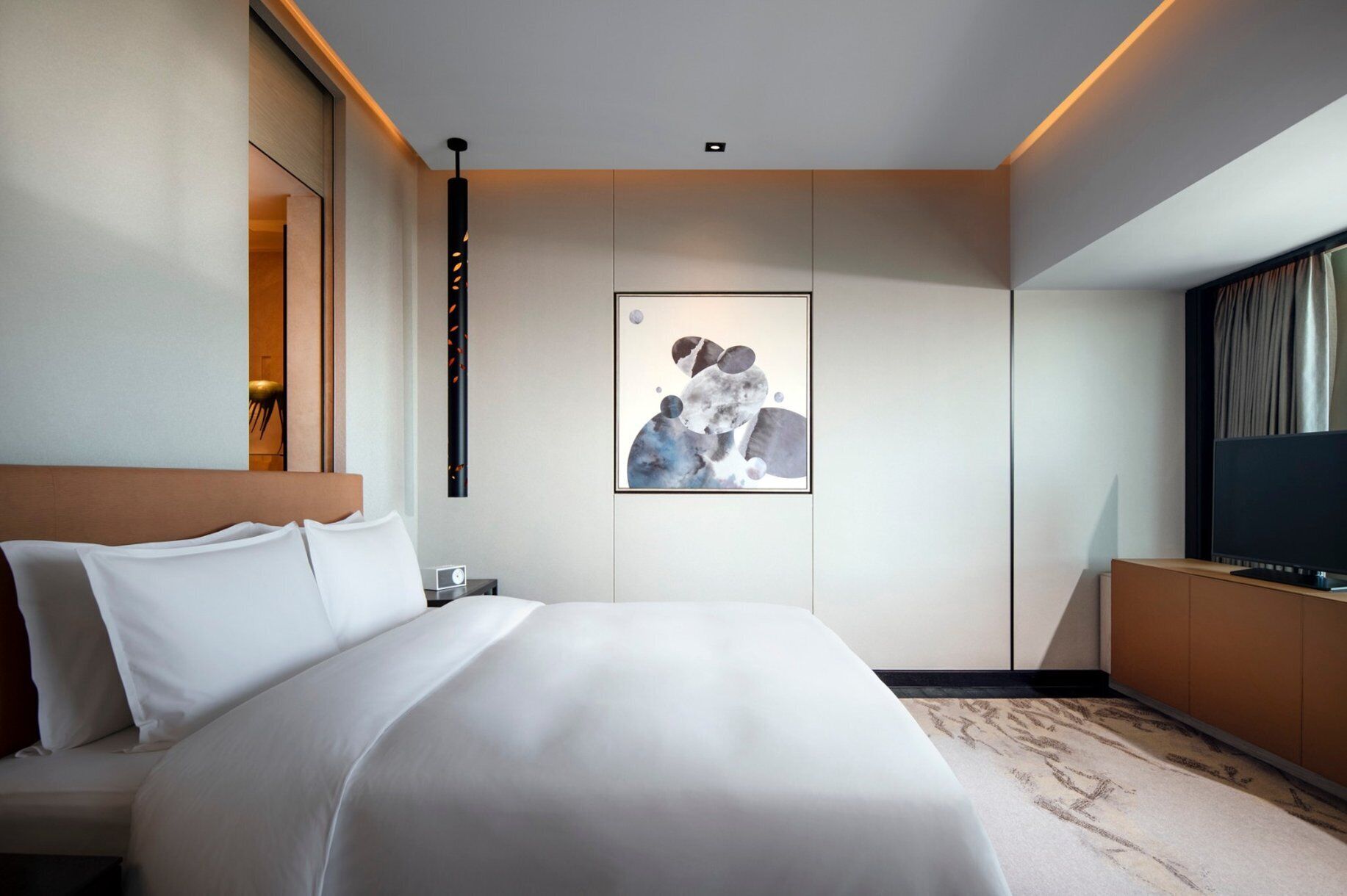 A modern hotel room with a large bed, a flat-screen TV, a painting on the wall, and a wooden headboard.
