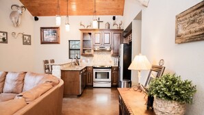 A cozy kitchen with wooden cabinets, a dining table with a lamp, and a sofa. - ANTLER OAKS CABIN  (San Saba)