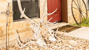 A stone building with a red door, a window with a decorative glass panel, and a large wheel mounted on the wall. - ANTLER OAKS CABIN  (San Saba)